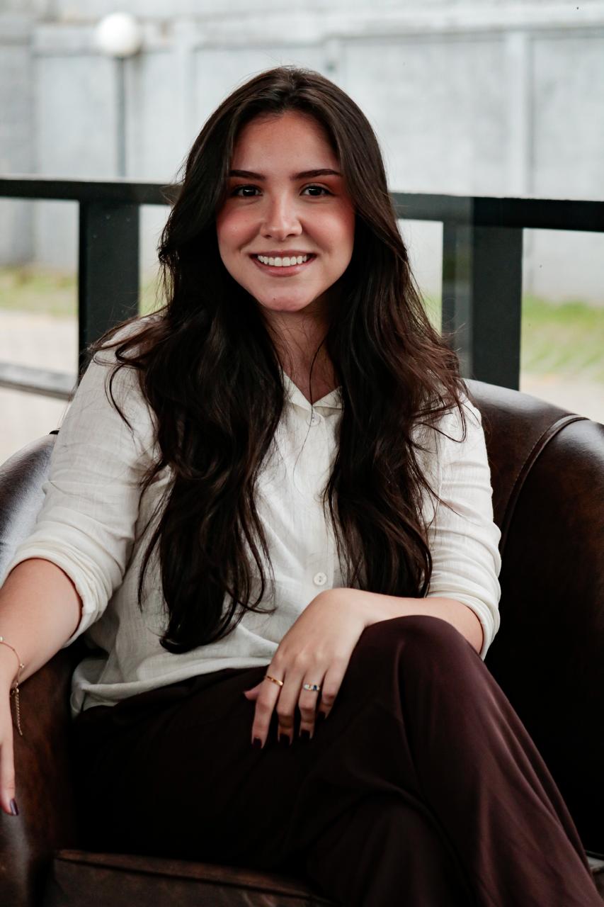 Ana Beatriz sorrindo, sentada em uma poltrona de couro